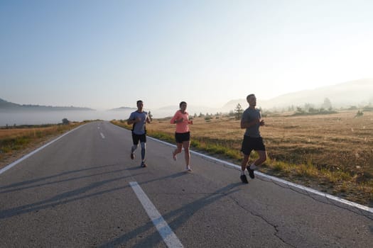 A group of friends, athletes, and joggers embrace the early morning hours as they run through the misty dawn, energized by the rising sun and surrounded by the tranquil beauty of nature.