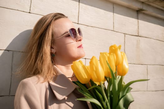 Woman holding yellow tulips, leaning against stone wall. Women's holiday concept, giving flowers