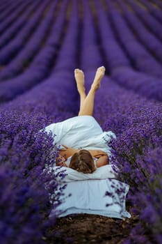 A middle-aged woman lies in a lavender field and enjoys aromatherapy. Aromatherapy concept, lavender oil, photo session in lavender.