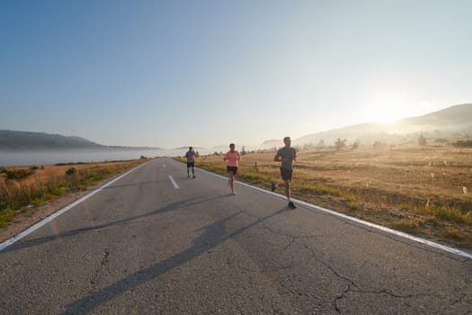 A group of friends, athletes, and joggers embrace the early morning hours as they run through the misty dawn, energized by the rising sun and surrounded by the tranquil beauty of nature.