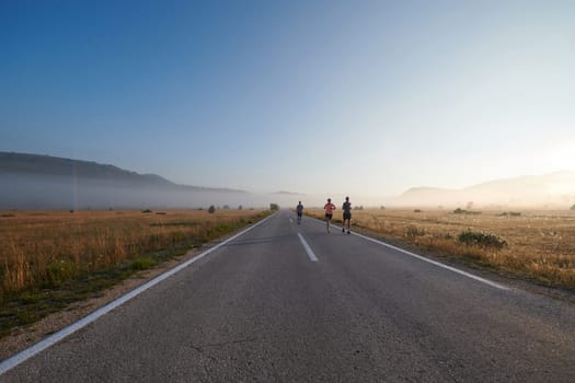 A group of friends, athletes, and joggers embrace the early morning hours as they run through the misty dawn, energized by the rising sun and surrounded by the tranquil beauty of nature.