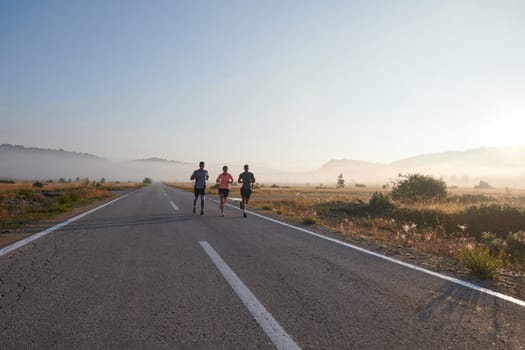 A group of friends, athletes, and joggers embrace the early morning hours as they run through the misty dawn, energized by the rising sun and surrounded by the tranquil beauty of nature.