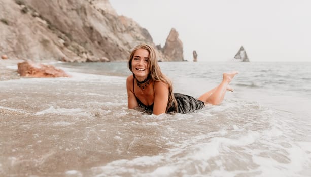 Woman travel sea. Young Happy woman in a long red dress posing on a beach near the sea on background of volcanic rocks, like in Iceland, sharing travel adventure journey