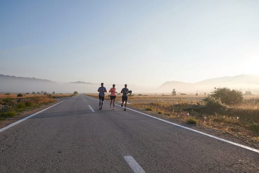 A group of friends, athletes, and joggers embrace the early morning hours as they run through the misty dawn, energized by the rising sun and surrounded by the tranquil beauty of nature.