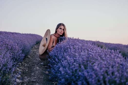 Close up portrait of young beautiful woman in a white dress and a hat is walking in the lavender field and smelling lavender bouquet.