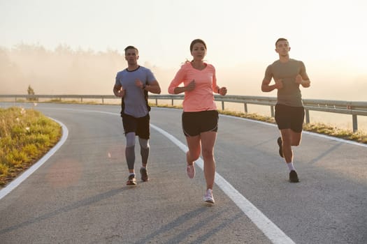 A group of friends, athletes, and joggers embrace the early morning hours as they run through the misty dawn, energized by the rising sun and surrounded by the tranquil beauty of nature.