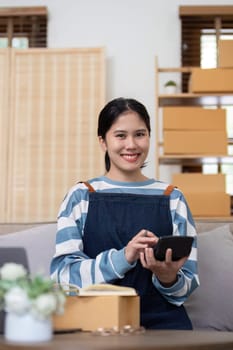 A young Asian entrepreneur sells product online through an online platform and pack product into shipping boxes..