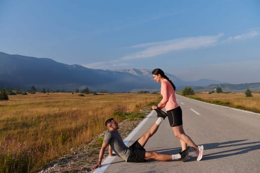 As dawn breaks, a romantic couple engages in a gentle stretch together, symbolizing their shared dedication and preparation for an invigorating early morning run.