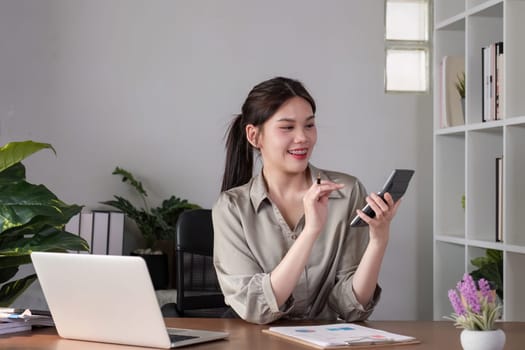 Young Asian business woman sitting in the office using a calculator to calculate business numbers..