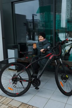An elderly woman is waiting for her friend with a bicycle on the street in winter.