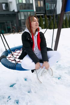 Carefree young woman riding on a swing in winter.