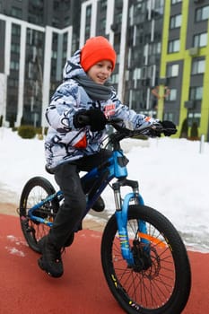 Caucasian boy dressed in a winter jacket rides a bicycle.