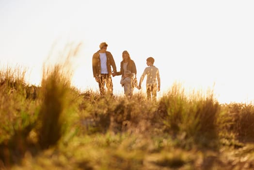 Family, grass and walk at sunset, nature and bonding with exercise for parents and children. Lens flare, autumn and hike on holiday in English countryside, mother and father for outdoor activity.