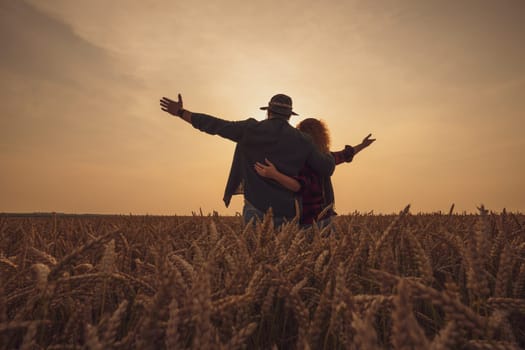 Man and woman are standing in their agricultural field in sunset. They are cultivating wheat and enjoying good agricultural season.