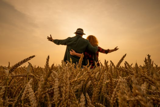 Man and woman are standing in their agricultural field in sunset. They are cultivating wheat and enjoying good agricultural season.