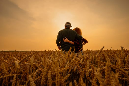 Man and woman are standing in their agricultural field in sunset. They are cultivating wheat and enjoying good agricultural season.