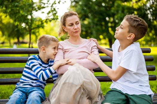 Mother is sitting with her sons on bench in park. She is angry and the boys try to apologize.