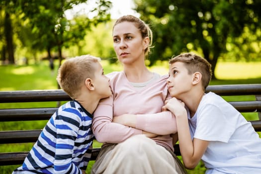 Mother is sitting with her sons on bench in park. She is angry and the boys try to apologize.