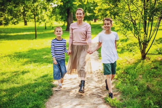 Happy mother is walking with her sons in park. They are holding hands and enjoying summer day.