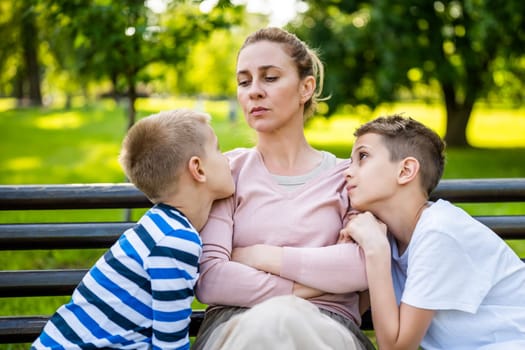 Mother is sitting with her sons on bench in park. She is angry and the boys try to apologize.