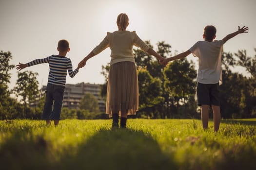 Happy mother is playing with her sons in park. They are holding hands and enjoying sunset.