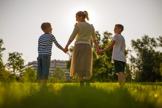 Happy mother is playing with her sons in park. They are holding hands and enjoying sunset.