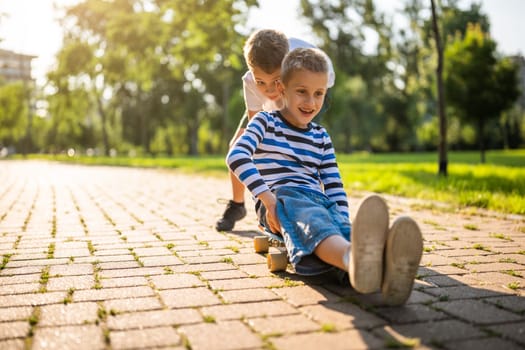 Two boys are having fun with skateboard in park. Playful children in park, happy childhood.