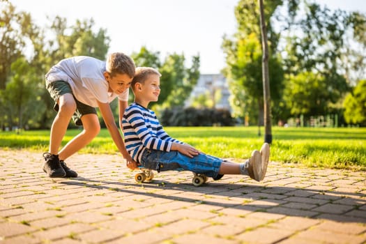 Two boys are having fun with skateboard in park. Playful children in park, happy childhood.