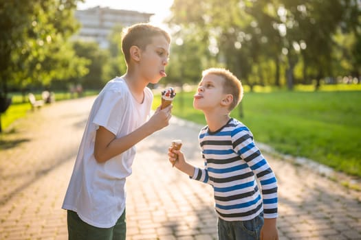 Two brothers are eating ice cream in park in summer. They are having fun and mocking at each other.