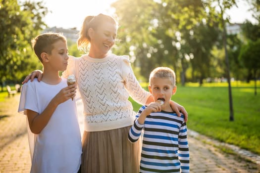 Portrait of happy single mother with her two sons in park on sunny day. Boys are eating ice cream.