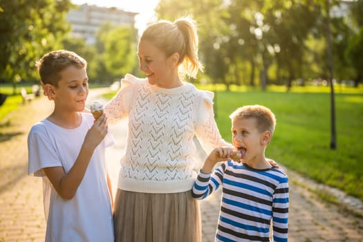 Portrait of happy single mother with her two sons in park on sunny day. Boys are eating ice cream.