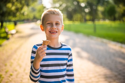 Portrait of happy boy who is standing in park and eating ice cream.