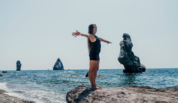 Woman travel sea. Young Happy woman in a long red dress posing on a beach near the sea on background of volcanic rocks, like in Iceland, sharing travel adventure journey