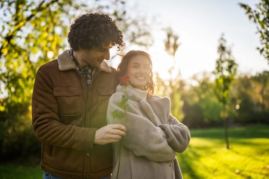 Portrait of happy loving couple in park in sunset. Man is giving rose to his woman.