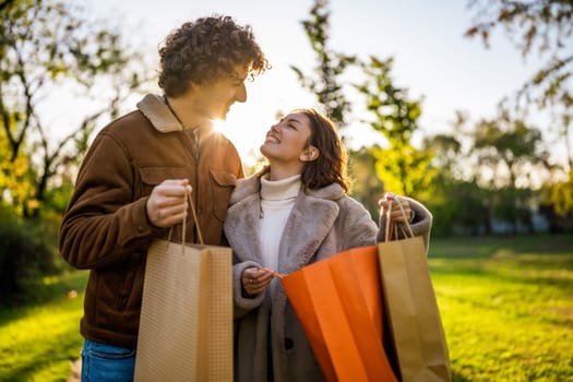 Portrait of happy loving couple in park in sunset. They are looking inside shopping bags.