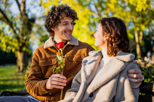 Portrait of happy loving couple in park. Man is giving rose to his woman.
