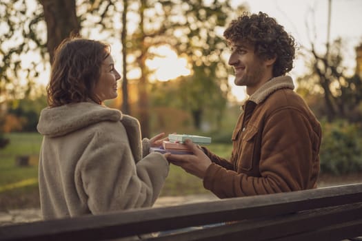 Happy loving couple enjoying their time together in park. Man is giving gift box to his woman.