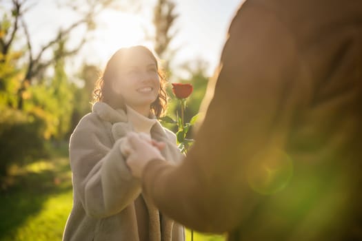 Portrait of happy loving couple in park in sunset. Man is giving rose to his woman.