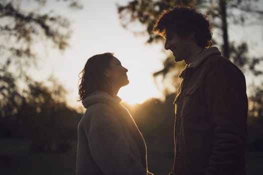 Portrait of happy loving couple in park in sunset. Couple in silhouette looking at each other.