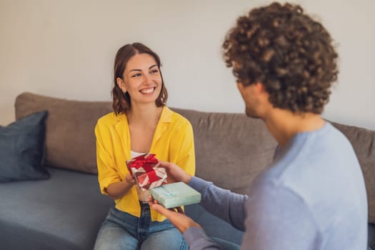 Portrait of young happy couple. Woman is giving gift to her man.