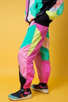 A fashionable girl in bright colorful retro-style clothes on a yellow background enjoys the atmosphere of the 80s and 90s.