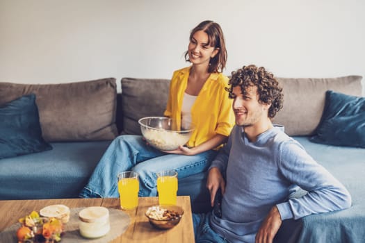 Portrait of young happy couple who is relaxing and watching TV at home.