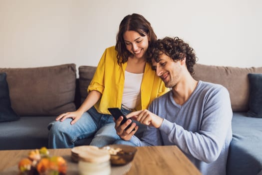 Portrait of young happy couple who is looking at smartphone at home.