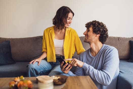 Portrait of young happy couple who is looking at smartphone at home.