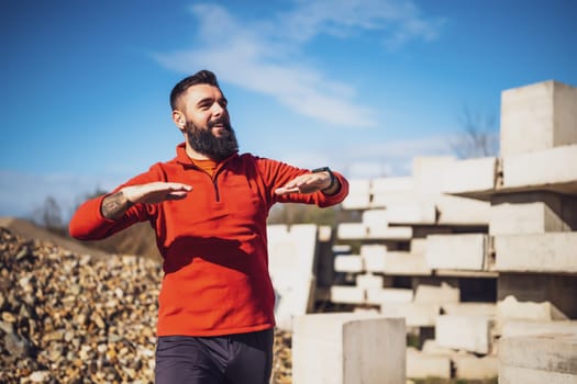 Adult man is exercising outdoor on sunny day. He is stretching his body.