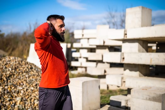 Adult man is exercising outdoor on sunny day. He is stretching his body.