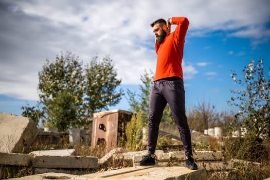 Adult man is exercising outdoor on sunny day. He is stretching his body.