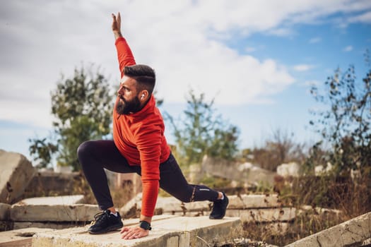 Adult man is exercising outdoor on sunny day. He is stretching his body.