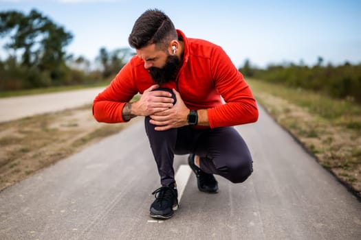 Young man is having pain in knee while exercising and jogging outdoor.