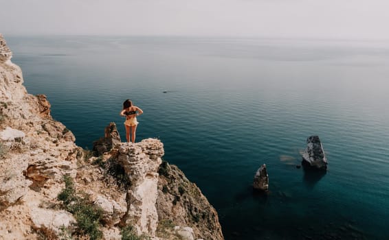 Woman travel sea. Happy tourist taking picture outdoors for memories. Woman traveler looks at the edge of the cliff on the sea bay of mountains, sharing travel adventure journey.